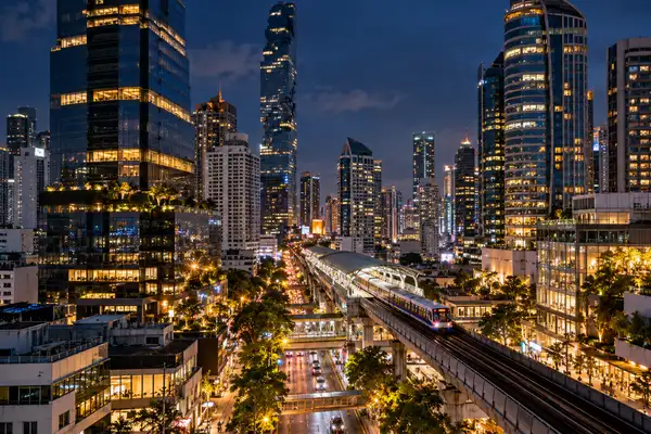 Bangkok skyline at night over Silom with lit office towers and a skytrain station