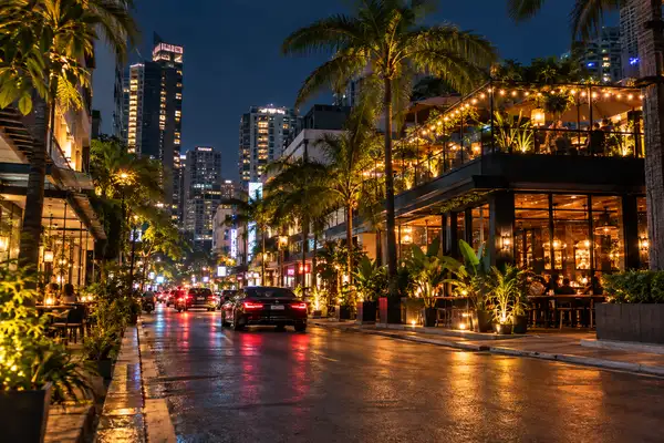 Lit street in Bangkok at night with palm trees, warm bar lights and a terrace above the road