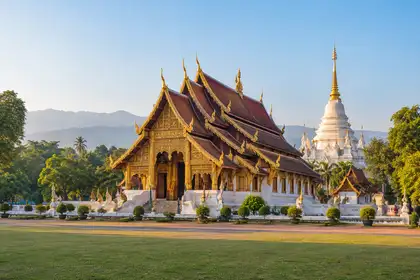 Golden tiered Lanna style temple roof with a white chedi behind it in morning light