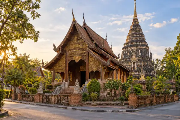 Old brick and teak temple with a tall dark chedi behind it on a quiet street