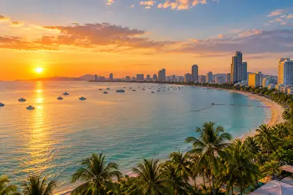 Curved Pattaya bay at golden hour with calm sea, palm trees and the city skyline along the shore