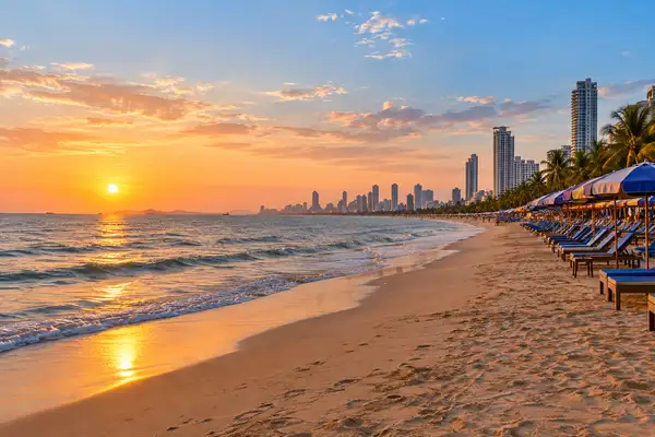 Long Jomtien Beach at golden hour with rows of beach chairs and condo towers along the coast