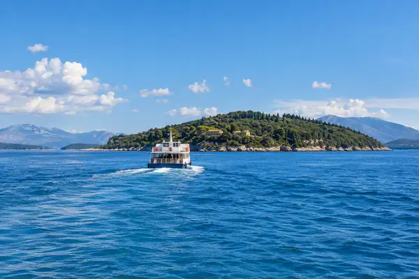 Small ferry boat crossing blue water toward a green island near Pattaya