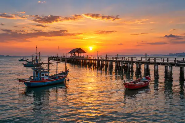 Naklua fishing pier at dusk with small colourful boats on calm water