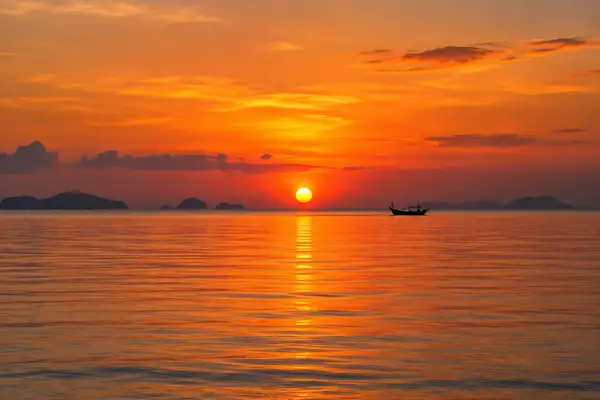 Orange sunset over the calm Gulf of Thailand with a small boat far away