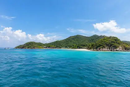 Small ferry boat crossing blue water toward the green hills of Koh Larn near Pattaya