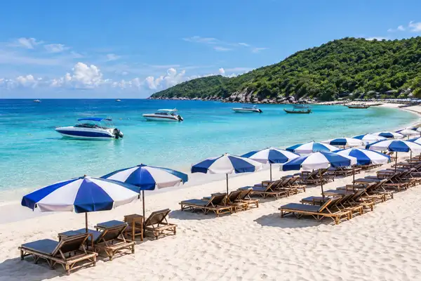 Tawaen Beach on Koh Larn with beach umbrellas, calm blue water and boats near the shore