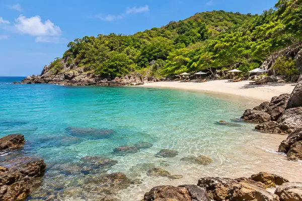 Small Tien Beach on Koh Larn with calm water, rocks at the edges and a few loungers