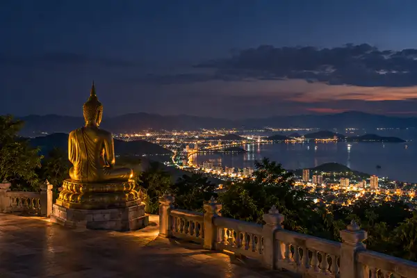 Indy Massage Pattaya: hilltop viewpoint at night over a lit coastal city with a Buddha statue in silhouette